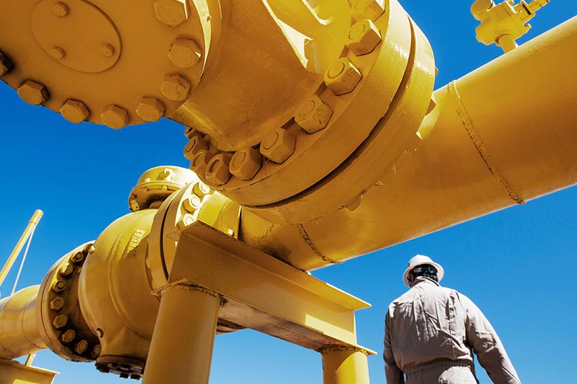 oil refinery worker standing next to yellow pipeline